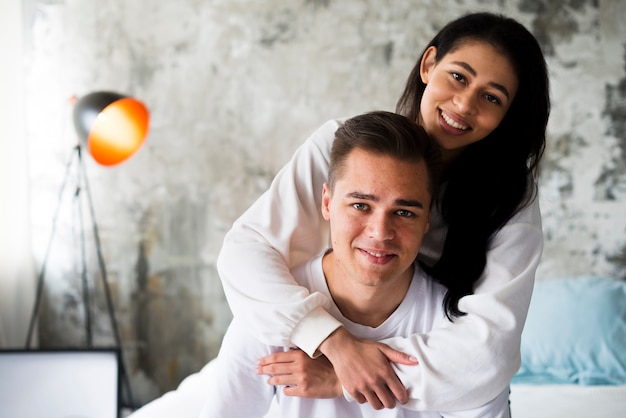 Sourire ethnique femme en vêtements blancs étreignant bel homme par derrière