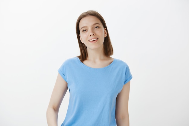 Sourire étudiant femme moderne avec expression heureuse debout sur un mur blanc