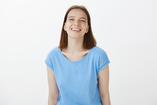 Sourire étudiant femme moderne avec expression heureuse debout sur un mur blanc