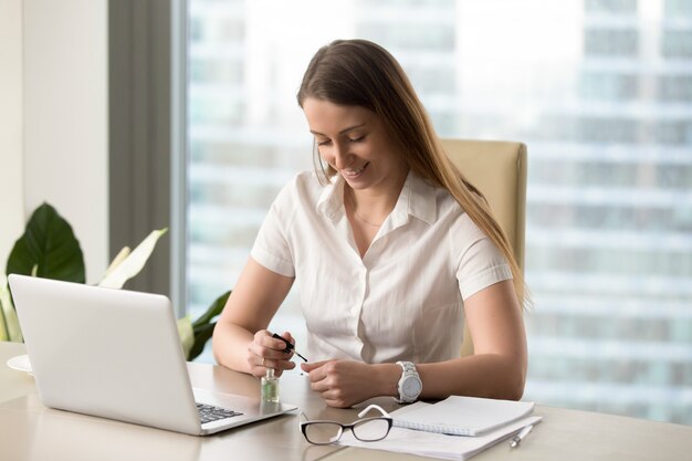 Sourire de femme d&#39;affaires peindre des ongles au bureau