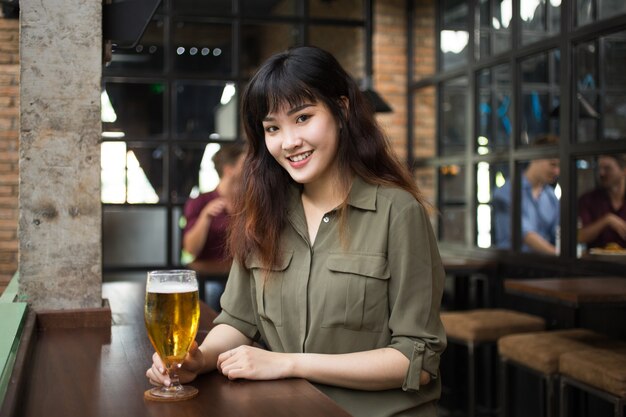 Sourire, femme asiatique, boire de la bière au pub