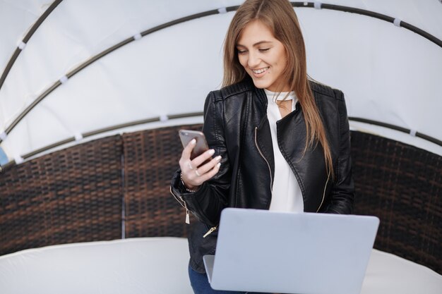 Sourire femme assise dans un fauteuil en osier regardant son téléphone