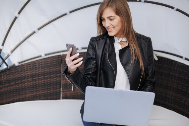 Sourire femme assise dans un fauteuil en osier regardant son téléphone