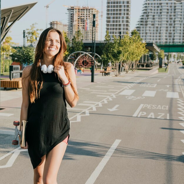 Sourire femme tenant skateboard marche dans la rue