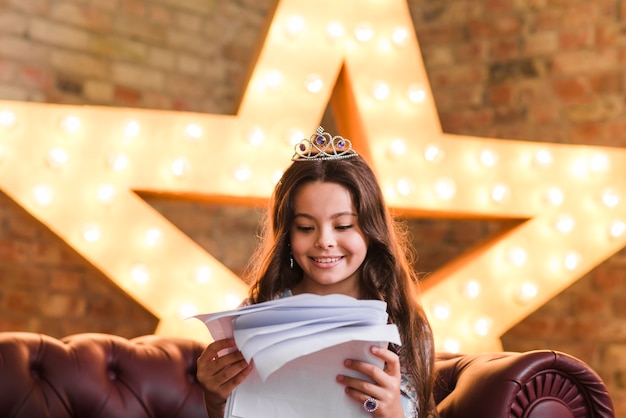 Photo gratuite sourire fille assise sur un canapé en lisant des scripts contre l'étoile rougeoyante en arrière-plan