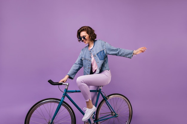 Sourire fille enchanteresse assise sur un vélo bleu. modèle féminin de bonne humeur
