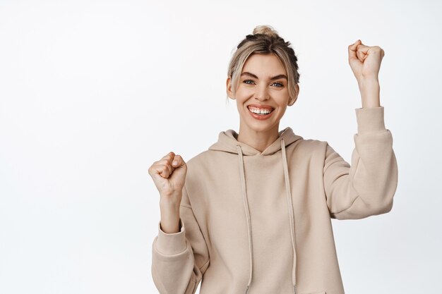 Sourire fille heureuse levant la main pour soutenir ou approuver quelqu'un, enracinement pour l'équipe, vous applaudissant, debout sur blanc