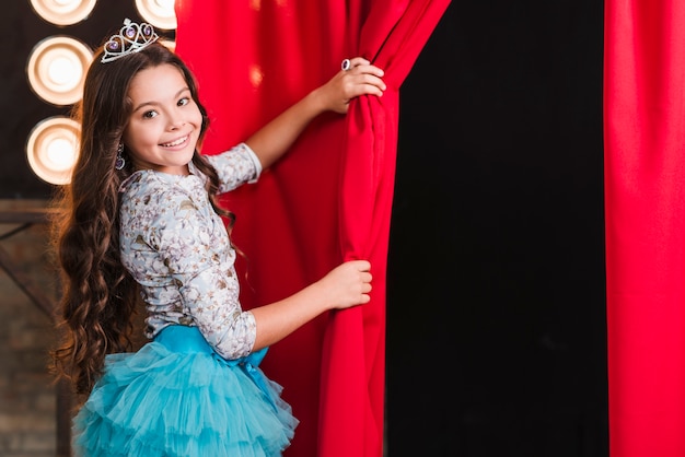 Sourire fille portant la couronne ouvrant le rideau rouge