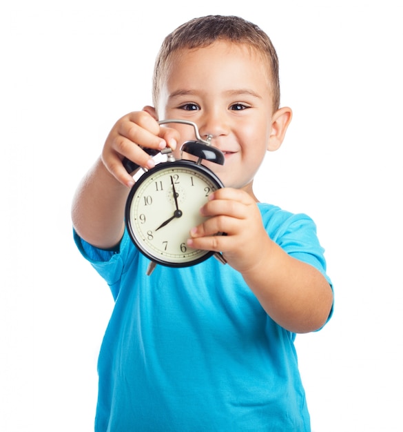 Sourire garçon montrant avec une horloge d&#39;alarme