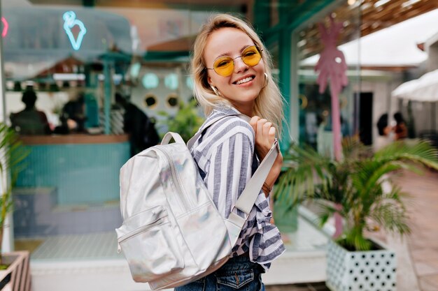 Sourire heureuse fille élégante dans des spectacles à la mode ronds portant chemise dépouillée