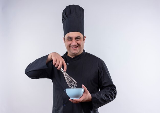 Sourire homme d'âge moyen cuisinier en uniforme de chef tenant un fouet et un bol