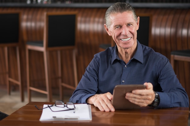 Sourire homme senior avec tablette numérique dans le café