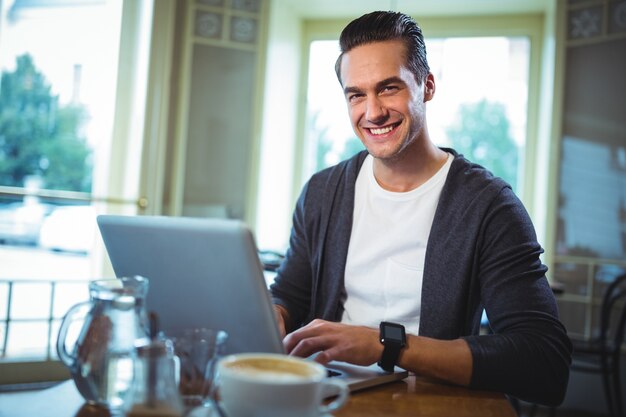 Sourire homme utilisant un ordinateur portable tout en ayant du café dans un café ©