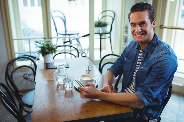 Sourire homme utilisant un téléphone portable dans un café ©