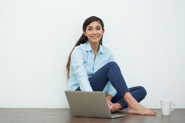 Sourire jeune femme avec un ordinateur portable et le thé à l&#39;étage