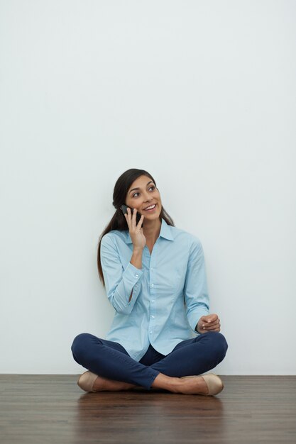 Sourire jeune femme parlant au téléphone sur le plancher