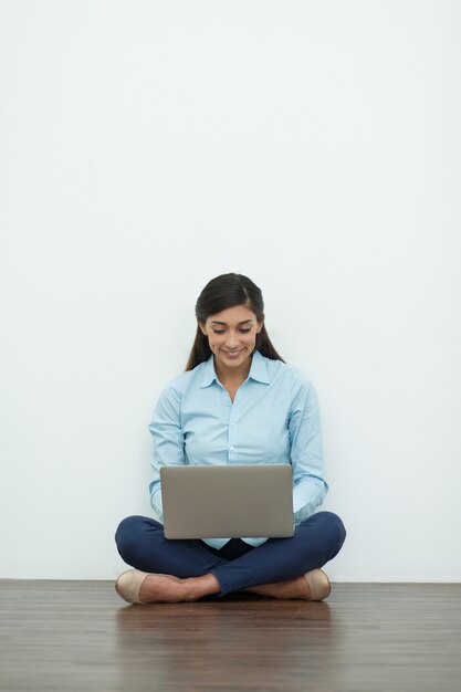 Sourire jeune femme travaillant sur un ordinateur portable sur le plancher