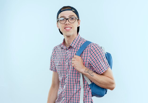 Sourire jeune garçon étudiant portant un sac à dos et des lunettes et une casquette sur blanc