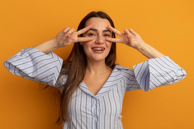 Sourire jolie femme caucasienne gestes signe de la main de la victoire avec deux mains et regarde à travers les doigts isolés