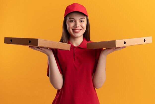 Sourire jolie femme de livraison en uniforme détient des boîtes de pizza sur les mains sur orange