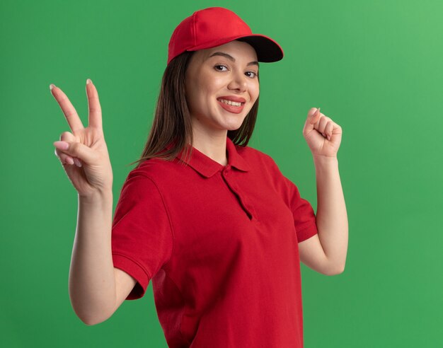 Sourire jolie femme de livraison en uniforme garde le poing et les gestes signe de la main de la victoire sur le vert