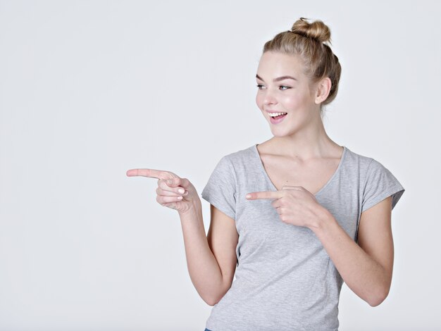 Sourire jolie femme pointant le doigt sur fond gris. Regarder la caméra