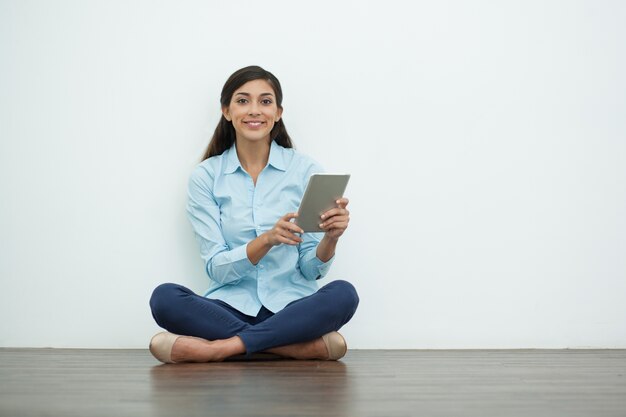 Sourire jolie femme avec tablette sur le plancher