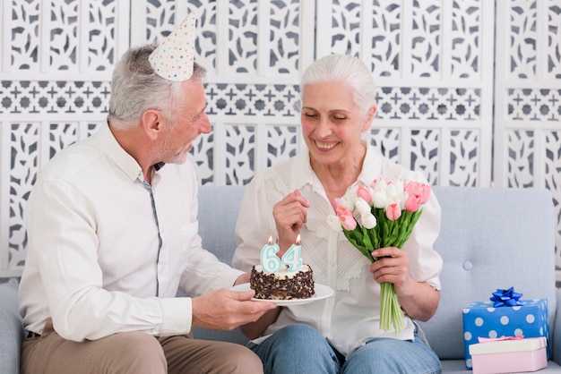 Sourire mari donnant le gâteau d'anniversaire à sa femme portant chapeau de fête