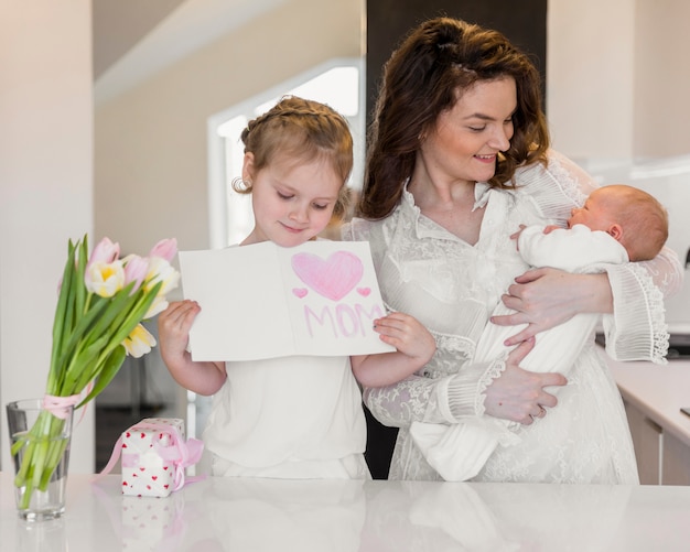 Sourire mère portant son bébé tandis que la fille tenant la carte de voeux