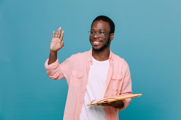 Sourire montrant bonjour geste tenant dossier jeune homme afro-américain isolé sur fond bleu