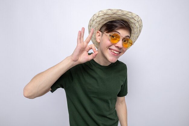 Sourire montrant un geste correct jeune beau mec portant un chapeau avec des lunettes