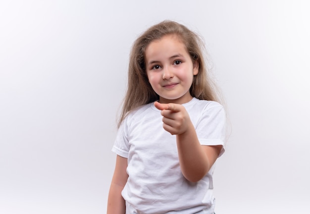 Sourire petite écolière portant un t-shirt blanc vous montrant le geste sur fond blanc isolé