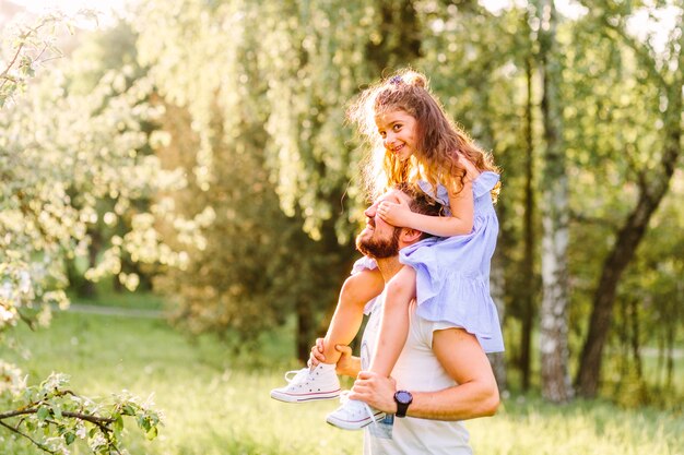 Sourire petite fille à cheval sur les épaules du père dans le parc