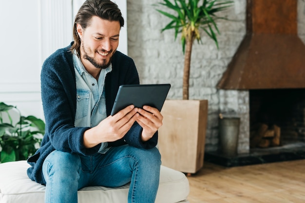 Sourire portrait d&#39;un bel homme assis sur un canapé en regardant tablette numérique