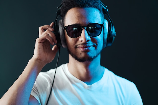 Sourire portrait de jeune homme afro-américain portant des écouteurs et écouter de la musique sur un mur noir