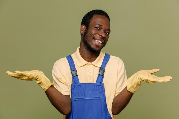 Sourire propagation mains jeune homme nettoyeur afro-américain en uniforme avec des gants isolés sur fond vert