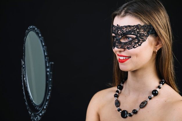 Photo gratuite sourire topless femme en masque de carnaval regardant dans la main miroir