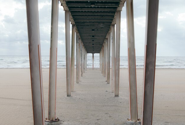 Sous une jetée en bois sur la plage de sable par temps nuageux