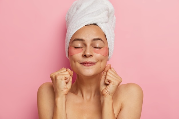 Spa femme fait un masque pour les cheveux, applique des patchs d'hydrogel, serre les poings comme anticipe pour l'effet du produit cosmétique, se tient torse nu avec les yeux fermés