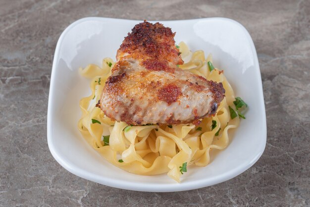 Spaghetti au poulet frit sur l'assiette, sur la surface en marbre.