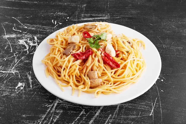 Spaghetti aux ingrédients mélangés dans une assiette blanche sur fond noir, vue du dessus.