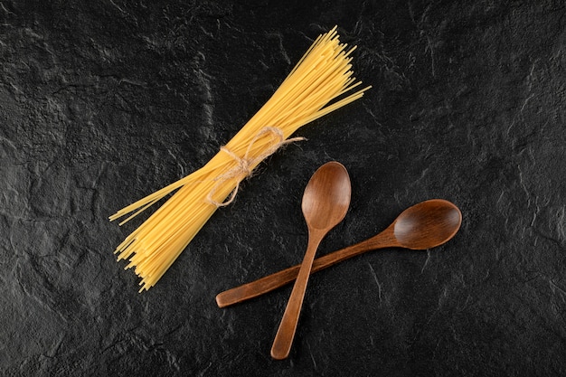Spaghetti crus et cuillères en bois sur une surface noire