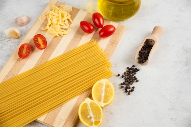 Spaghetti crus, huile et légumes frais sur planche de bois.