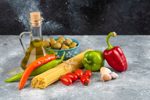 Spaghetti, huile et divers légumes sur table en pierre.