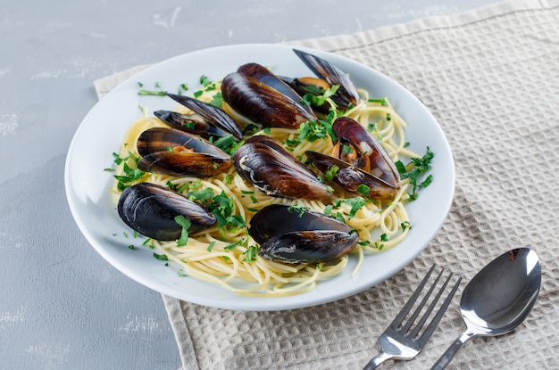 Photo gratuite spaghetti et moule avec cuillère, fourchette dans une assiette sur plâtre et torchon