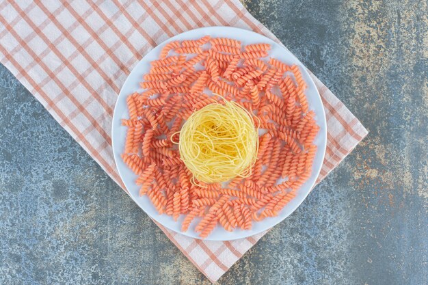 Spaghetti non cuit et pâtes fusilli dans un bol sur une serviette, sur le fond de marbre.