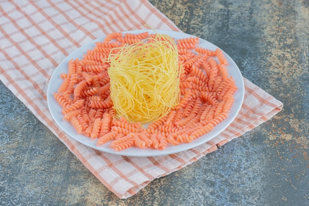 Spaghetti non cuits et pâtes fusilli dans un bol sur une serviette, sur la surface en marbre.