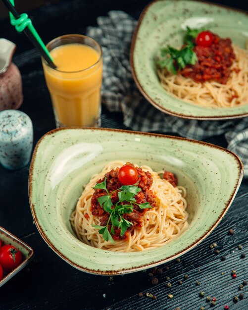 Spaghetti à la sauce bolognaise, herbes et tomates en plaque verte et jus d'orange autour.