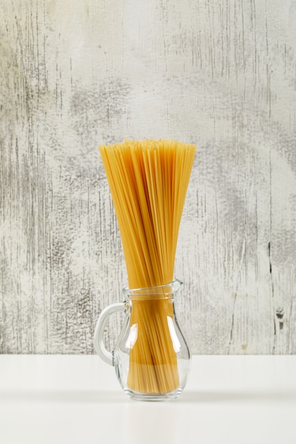 Spaghetti sec dans une mini cruche en verre vue latérale sur fond blanc et grunge