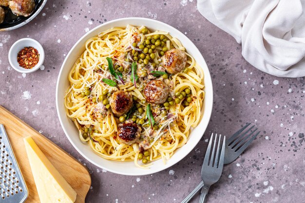 Des spaghettis avec des boulettes de viande et de la sauce à la crème sont servis sur une assiette avec des herbes et du parmesan